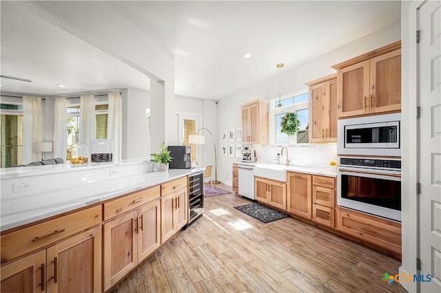 kitchen with light wood finished floors, light countertops, a sink, beverage cooler, and white appliances