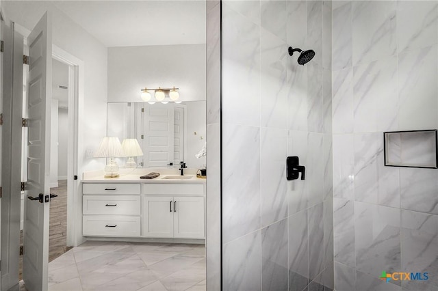 bathroom featuring marble finish floor, a tile shower, and vanity