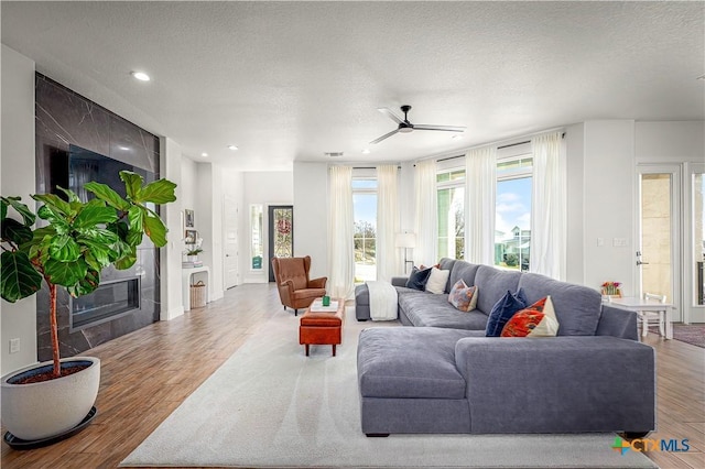 living room featuring a fireplace, recessed lighting, a ceiling fan, a textured ceiling, and wood finished floors