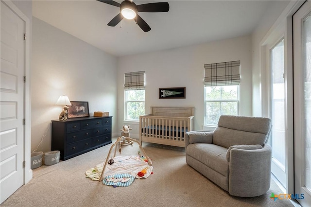 carpeted bedroom with a crib and a ceiling fan