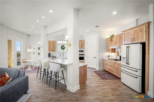 kitchen featuring high end fridge, light countertops, open floor plan, wood finished floors, and under cabinet range hood