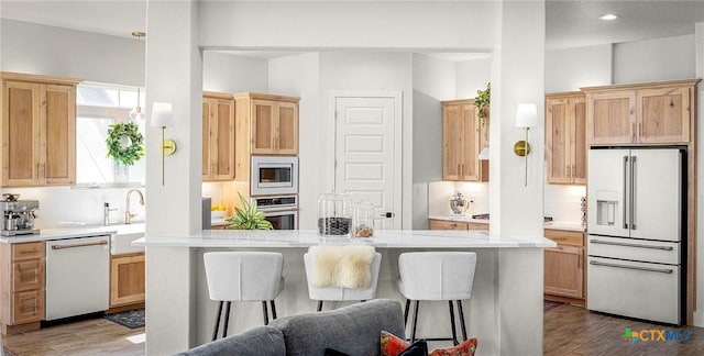 kitchen with appliances with stainless steel finishes, light countertops, wood finished floors, and light brown cabinetry