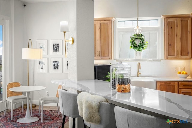 kitchen with a breakfast bar, brown cabinets, decorative light fixtures, decorative backsplash, and a sink