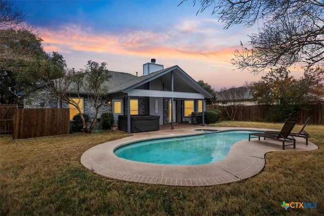 pool at dusk featuring a hot tub, a lawn, and a patio area