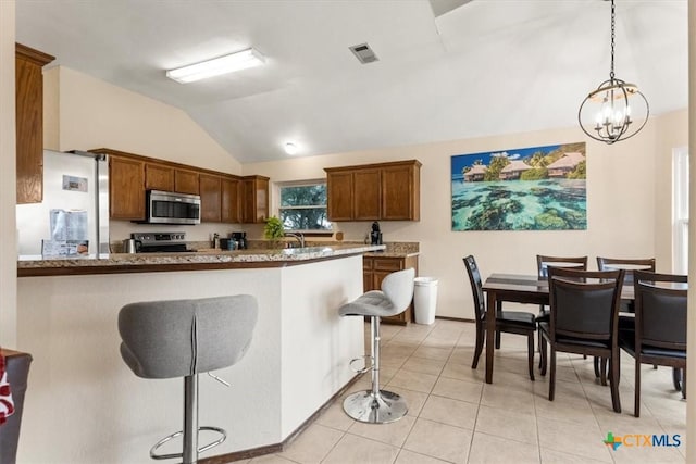 kitchen featuring appliances with stainless steel finishes, a breakfast bar, hanging light fixtures, light tile patterned floors, and kitchen peninsula