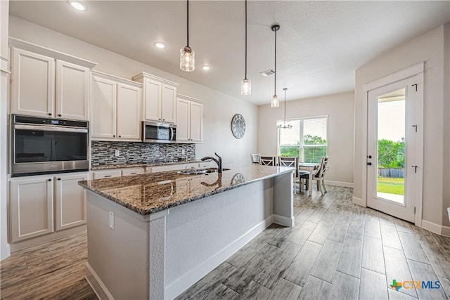 8508 Mount Nebo Cir, Belton, TX 76513 - kitchen with stainless steel appliances, a sink, light wood finished floors, dark stone counters, and decorative backsplash