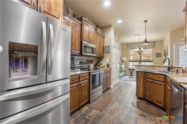 kitchen featuring brown cabinetry, dark wood-style flooring, appliances with stainless steel finishes, pendant lighting, and backsplash