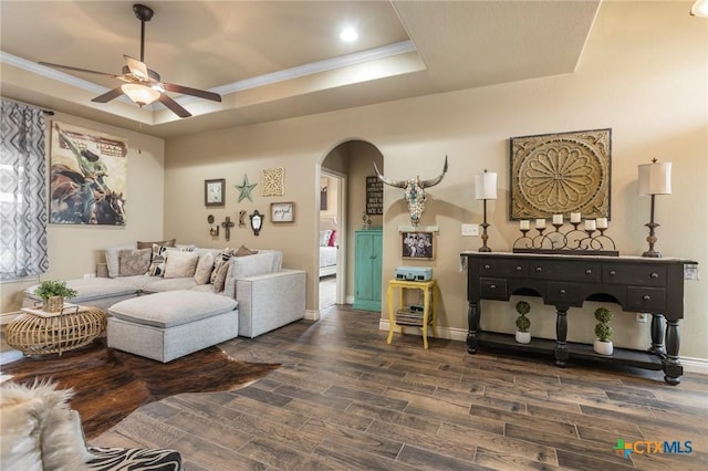 living area featuring a raised ceiling, arched walkways, dark wood-style flooring, and ornamental molding