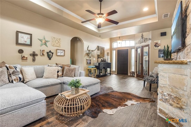 living room featuring a tray ceiling, arched walkways, wood tiled floor, and crown molding