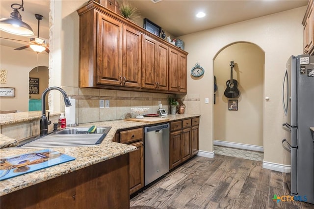 kitchen featuring dark wood-type flooring, a sink, backsplash, arched walkways, and appliances with stainless steel finishes