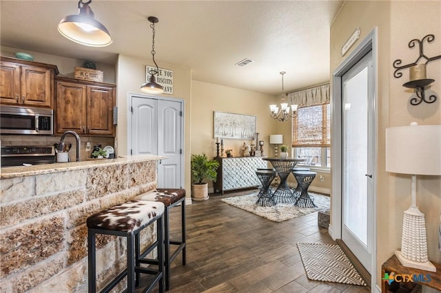 kitchen with dark wood-type flooring, pendant lighting, a notable chandelier, electric stove, and stainless steel microwave