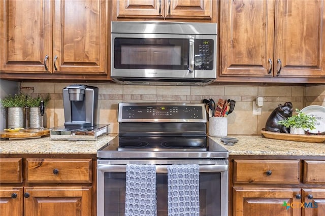 kitchen featuring light stone counters, backsplash, brown cabinetry, and appliances with stainless steel finishes