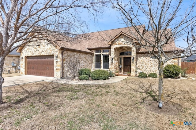 view of front facade featuring an attached garage, fence, roof with shingles, stone siding, and driveway