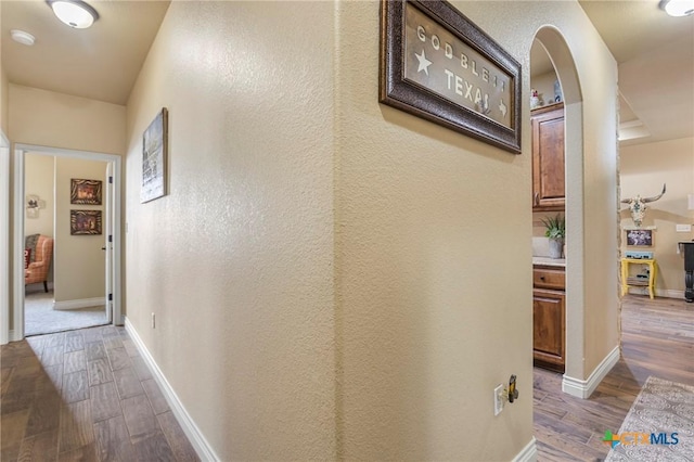 hallway with wood finished floors, baseboards, and arched walkways