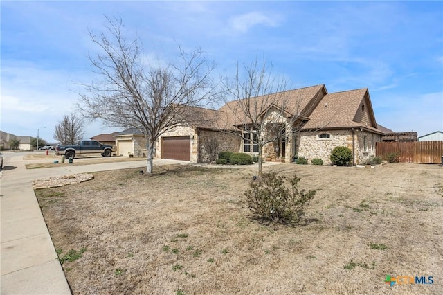 view of front of home featuring stone siding, driveway, an attached garage, and fence