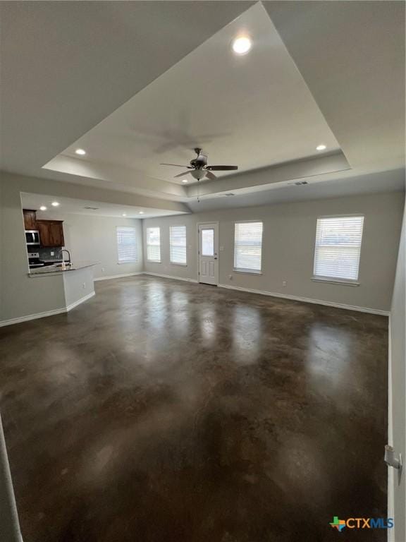 unfurnished living room with finished concrete flooring, a raised ceiling, and baseboards