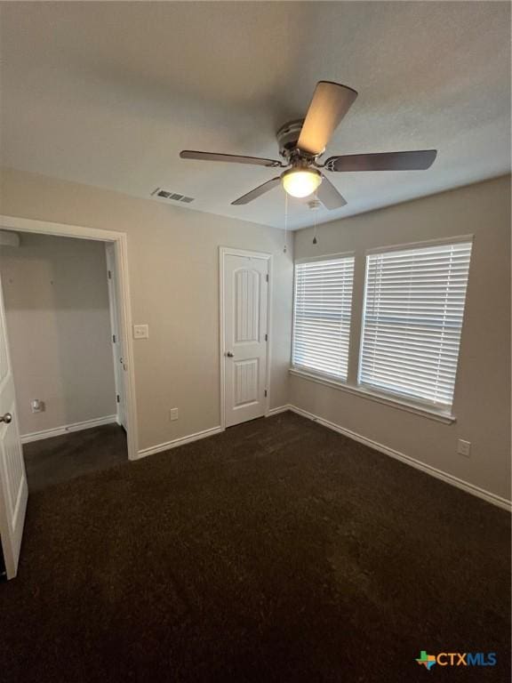 unfurnished bedroom with a ceiling fan, visible vents, dark colored carpet, and baseboards