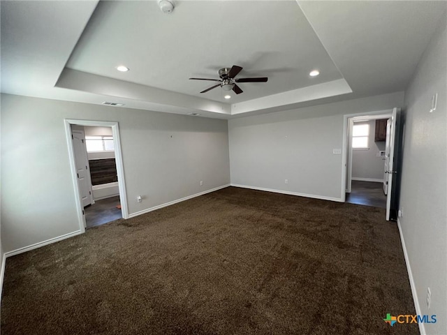 unfurnished bedroom with a tray ceiling, baseboards, and dark carpet