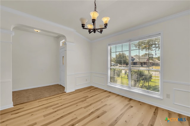 unfurnished dining area with a decorative wall, a wainscoted wall, wood finished floors, ornamental molding, and an inviting chandelier