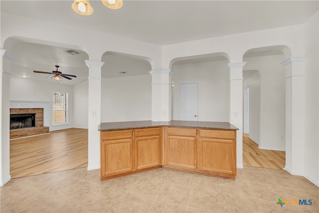 kitchen with light hardwood / wood-style flooring, a stone fireplace, ceiling fan, and dark stone counters