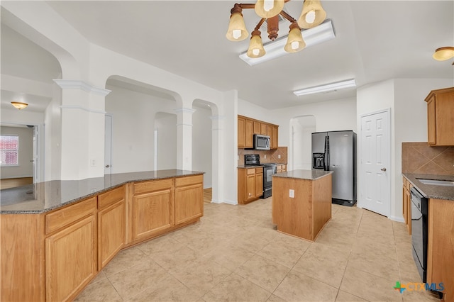 kitchen with decorative backsplash, decorative columns, black appliances, dark stone countertops, and a kitchen island