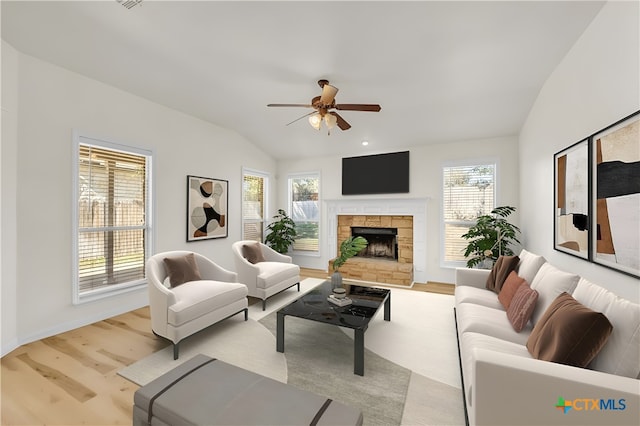 living room with ceiling fan, vaulted ceiling, a fireplace, and light hardwood / wood-style flooring