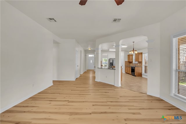 unfurnished living room featuring decorative columns, a wealth of natural light, a chandelier, and light wood-type flooring