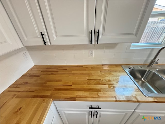 room details with white cabinets, wood counters, backsplash, and sink