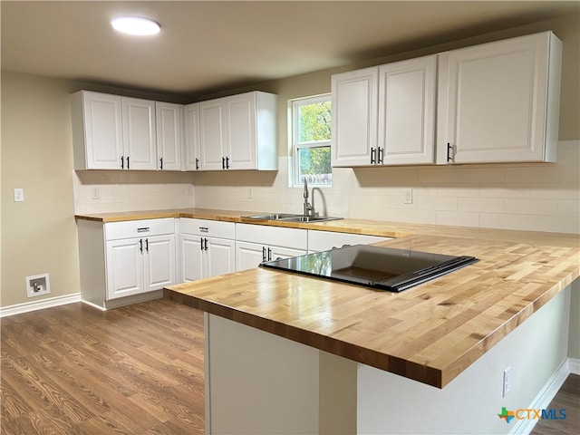 kitchen with kitchen peninsula, sink, light hardwood / wood-style floors, white cabinetry, and butcher block counters