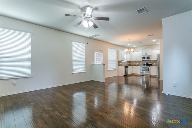 unfurnished living room with dark hardwood / wood-style flooring, a healthy amount of sunlight, and ceiling fan with notable chandelier