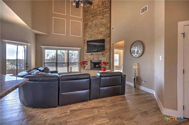 living room with a towering ceiling, a stone fireplace, and ceiling fan