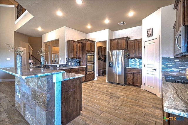 kitchen with dark brown cabinets, stainless steel appliances, light stone counters, and tasteful backsplash