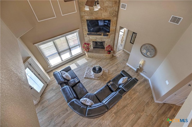 living room featuring a towering ceiling, a stone fireplace, ceiling fan, and plenty of natural light