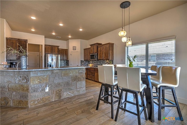 kitchen with hanging light fixtures, stainless steel appliances, decorative backsplash, a breakfast bar, and light wood-type flooring