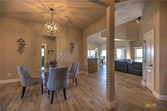 dining room with a textured ceiling, ceiling fan with notable chandelier, wood-type flooring, and lofted ceiling