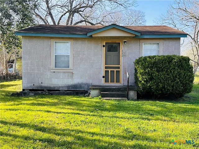 bungalow featuring entry steps, a front lawn, roof with shingles, and concrete block siding