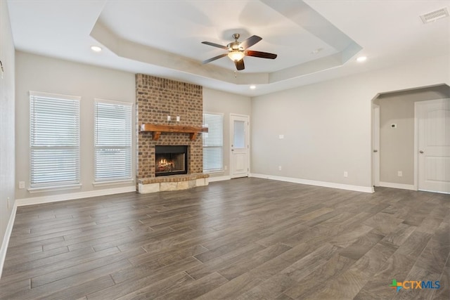 unfurnished living room featuring ceiling fan, a tray ceiling, dark hardwood / wood-style floors, and a fireplace