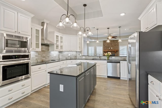 kitchen with pendant lighting, appliances with stainless steel finishes, wall chimney exhaust hood, and white cabinets