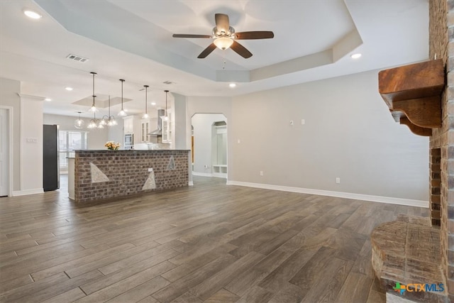 unfurnished living room featuring ceiling fan, dark hardwood / wood-style flooring, and a tray ceiling