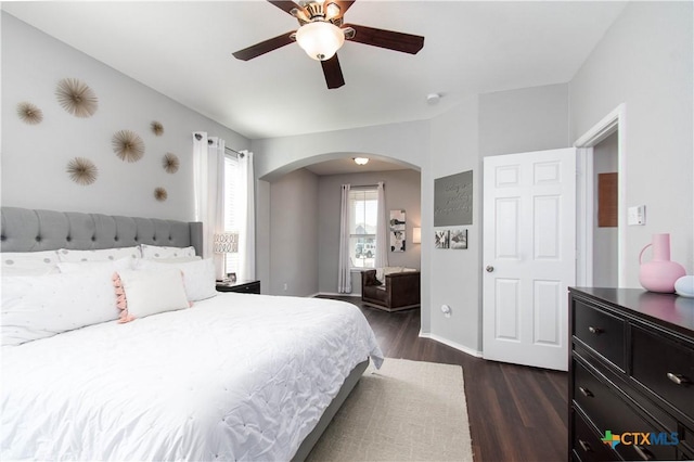 bedroom with dark wood-type flooring, arched walkways, ceiling fan, and baseboards