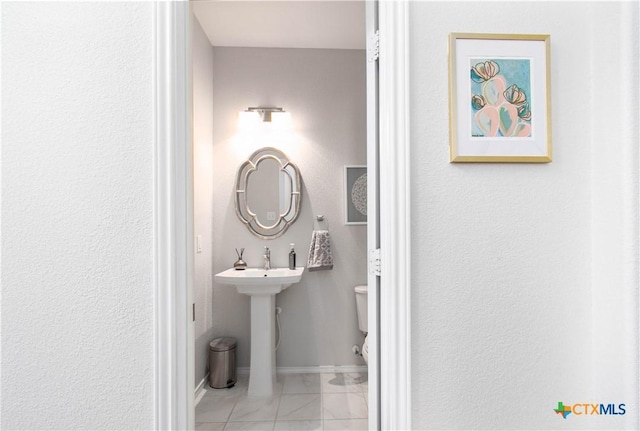 half bath with marble finish floor, baseboards, and toilet