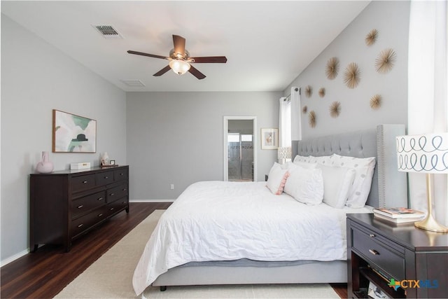 bedroom featuring dark wood finished floors, visible vents, a ceiling fan, ensuite bath, and baseboards