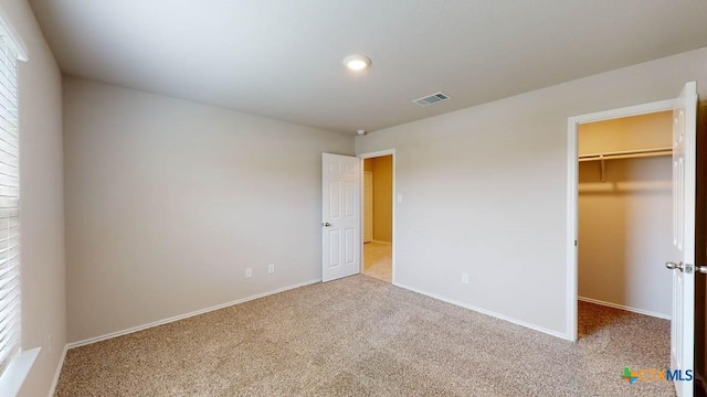 unfurnished bedroom with a spacious closet, carpet floors, visible vents, and baseboards