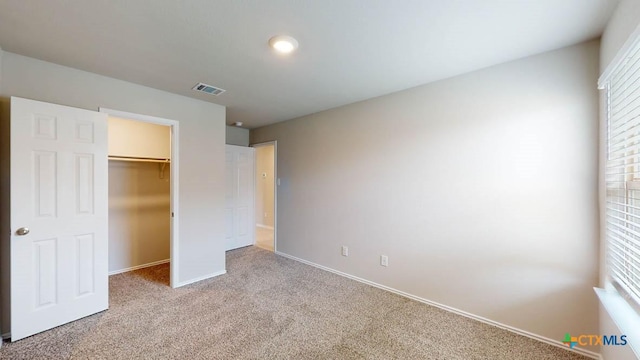 unfurnished bedroom with light carpet, multiple windows, a walk in closet, and visible vents