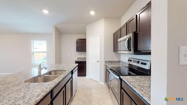 kitchen with appliances with stainless steel finishes, a sink, light stone counters, and dark brown cabinetry