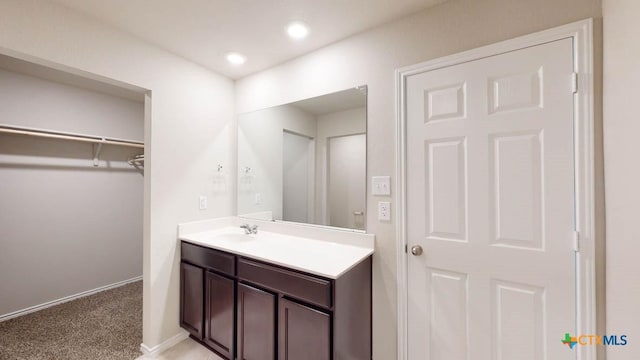 bathroom featuring recessed lighting, vanity, baseboards, and a spacious closet