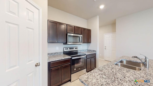 kitchen featuring stainless steel appliances, a sink, light stone counters, and dark brown cabinets