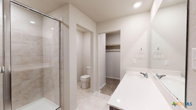 bathroom featuring toilet, a sink, a spacious closet, double vanity, and a stall shower