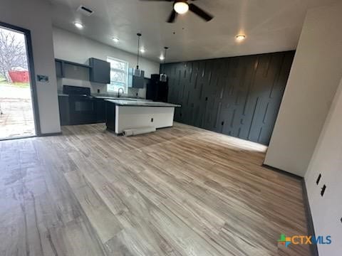 kitchen featuring wooden walls, a kitchen island, visible vents, open floor plan, and light wood-type flooring