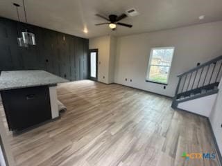 unfurnished living room featuring a ceiling fan, light wood-type flooring, visible vents, and stairway